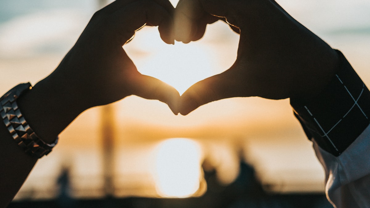 Two hands forming a heart shape against a golden sunset