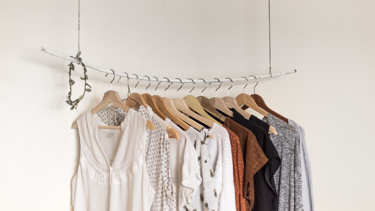 A rack of light blouses and tops on wooden hangers